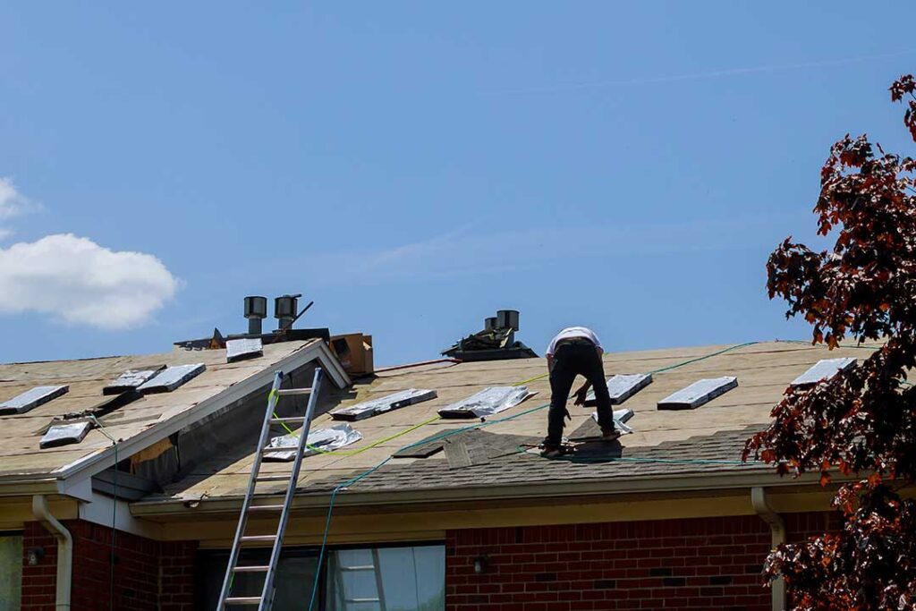 A homeowner using a ladder to inspect shingles and gutters for storm damage on a residential roof.