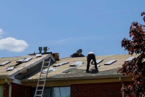 A homeowner using a ladder to inspect shingles and gutters for storm damage on a residential roof.
