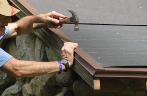 A homeowner checking roof shingles and clearing leaves from roof gutters on a sunny day.